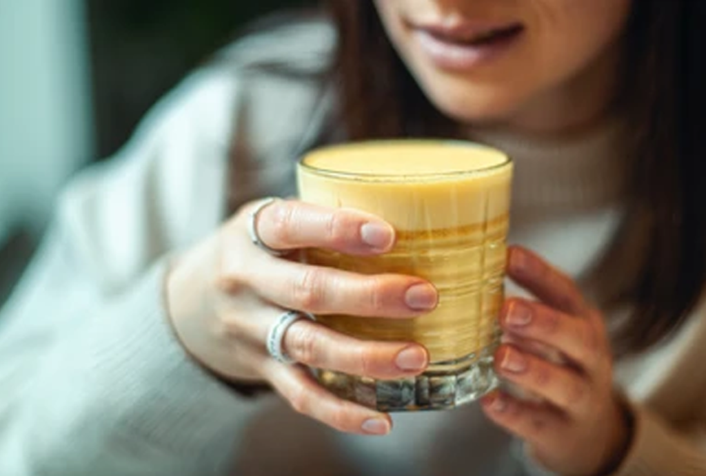 Happy Pakistani woman drinking turmeric milk with smile – supporting women's health and gynaecological well-being naturally – Hamza The Dietitian
